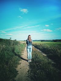 Rear view of woman walking on field against sky