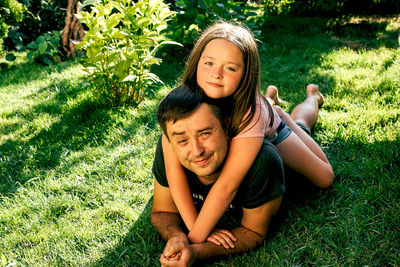 Portrait of father and daughter relaxing on grass outdoors