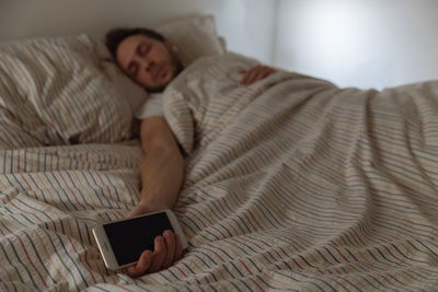 Man using mobile phone while lying on bed at home