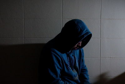 Man wearing hooded shirt sitting by wall