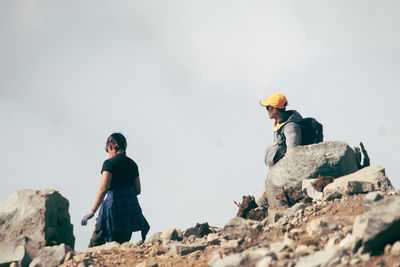 Rear view of man sitting on rock against clear sky