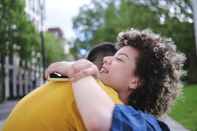 Happy young woman with eyes closed hugging boyfriend at park