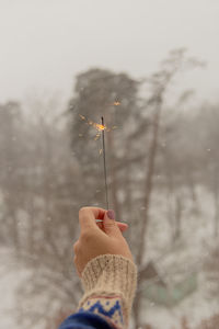 Woman's hand holds sparkle during snowfall with views of nature and houses