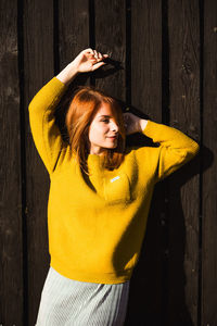 Beautiful young woman in yellow sweater standing against fence