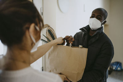 Man delivering groceries to woman standing at doorway during pandemic