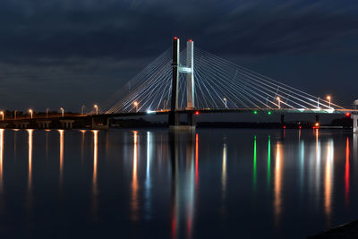Illuminated cable-stayed bridge over river against sky at night