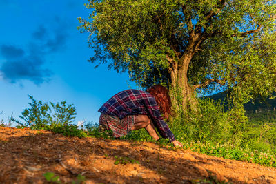 Rear view of woman walking by tree against blue sky