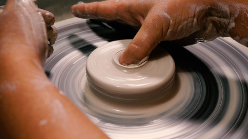 A potter's stained hands shape a stunning pot from white clay on the wheel. working in a pottery