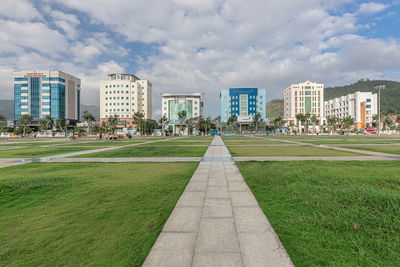 Park by buildings in city against sky