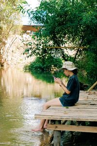 Side view of woman sitting on wood against trees