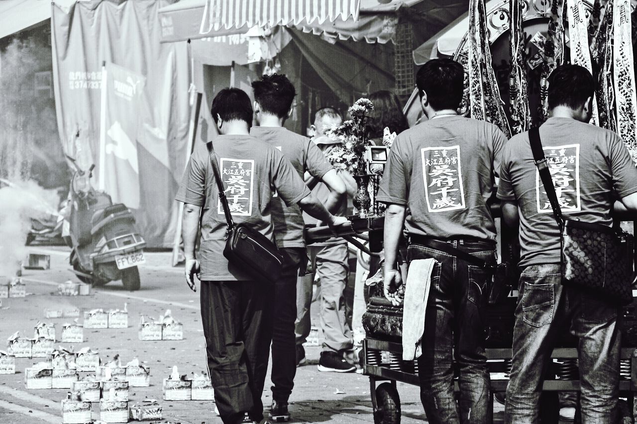 REAR VIEW OF PEOPLE STANDING ON STREET MARKET IN CITY