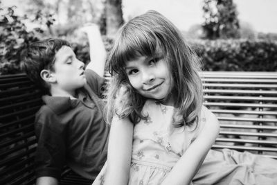 Portrait of smiling girl with brother sitting on bench
