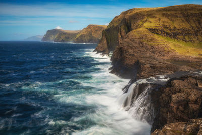 Waves splashing on rock formation at sea against sky