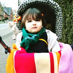 Cute toddler sitting in baby stroller on sidewalk at town