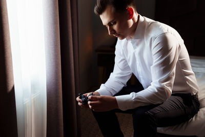 Young man using mobile phone while sitting on window