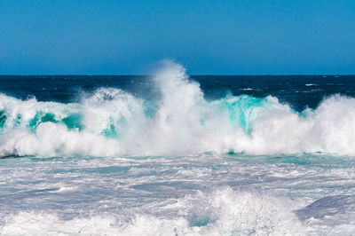 Impressive large ocean wave with white foam against deep blue of ocean and sky