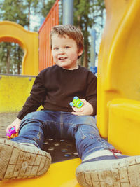 Portrait of cute boy holding toys while sitting on outdoor play equipment