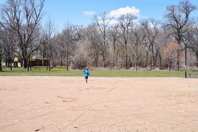 Full length of boy running on dirt road against bare trees