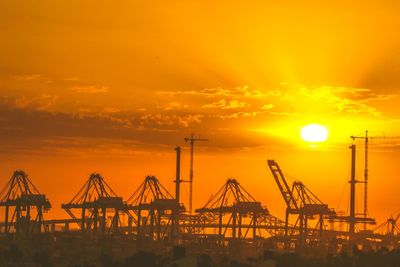 Cranes at harbor against orange sky