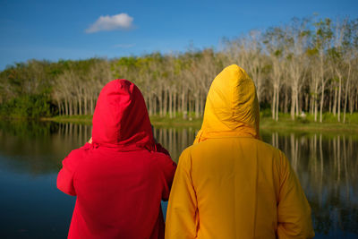Rear view of female friends standing by lake against trees