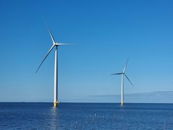 Wind turbines by sea against clear blue sky