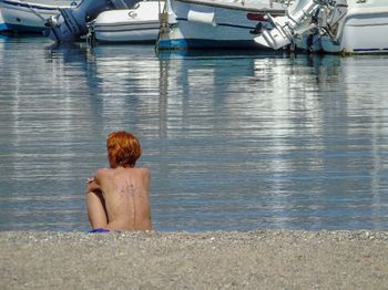 Rear view of shirtless woman sitting in sea