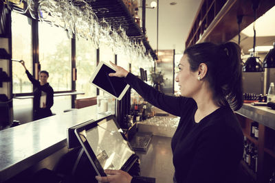 Side view of coworker pointing while talking to owner in cafe