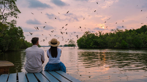 Rear view of woman sitting on pier over lake