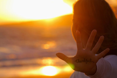 Woman showing thankful text on her palm at beach during sunset