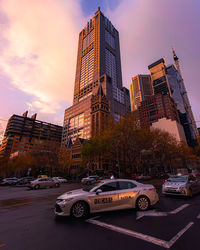 Cars on street by buildings against sky during sunset