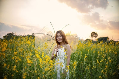 Woman standing by yellow flowers on field against sky