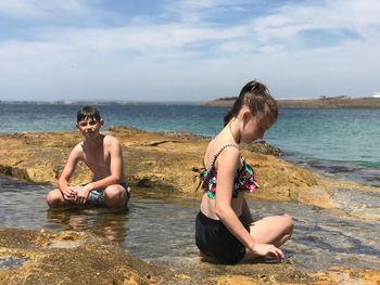 Happy friends sitting on shore against sky