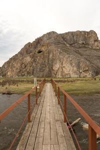 Wooden footbridge leading towards mountains against sky