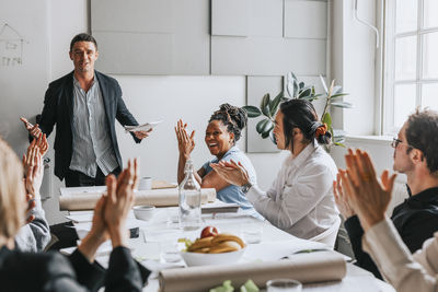 Male and female business people applauding for manager during meeting at work place