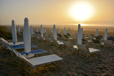 Chairs on beach against sky during sunset