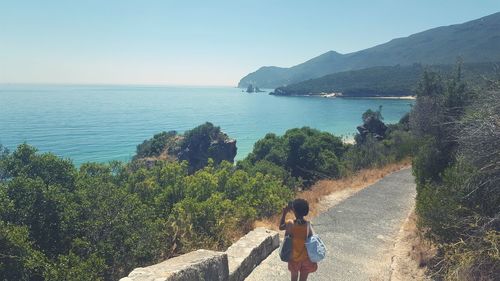 High angle view of woman standing on pathway amidst trees by sea against sky