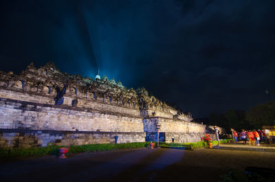 Road by illuminated buildings against sky at night