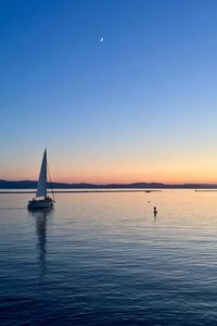 Sailboat sailing on sea against clear sky during sunset