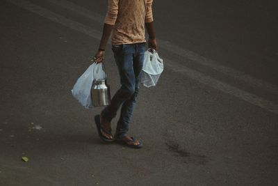 Low section of man carrying plastic bags while walking on road