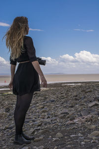 Side view of woman standing at beach against blue sky