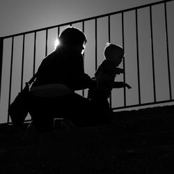 Low angle view of silhouette mother and son standing by railing on sunny day