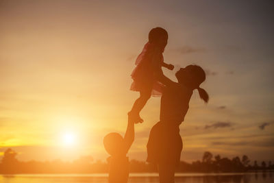 Silhouette mother and daughter against sky during sunset