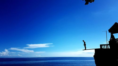 Silhouette man standing by sea against clear blue sky