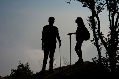 Low angle view of silhouette couple hiking on mountain against sky
