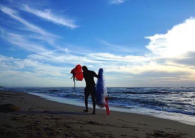 Fisherman walking at beach against sky