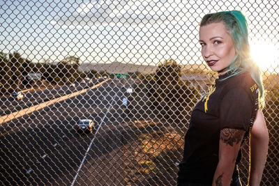 Portrait of woman standing by chainlink fence