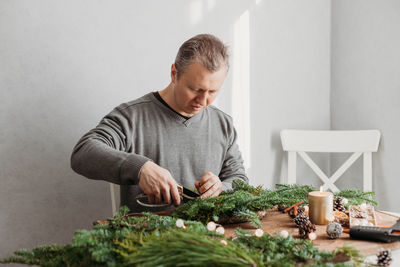 A man at home makes a christmas wreath from fresh spruce branches. decorating your home 