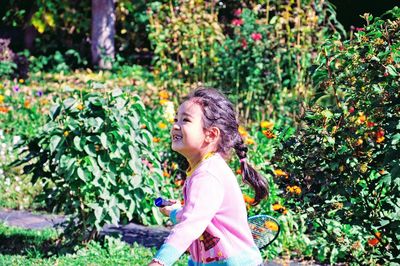 Side view of smiling girl playing badminton against plants