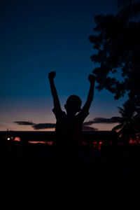 Silhouette woman with arms raised at sunset