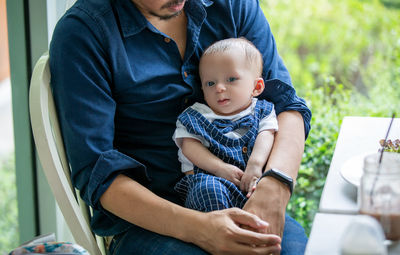 Midsection of father carrying cute son while sitting in cafe